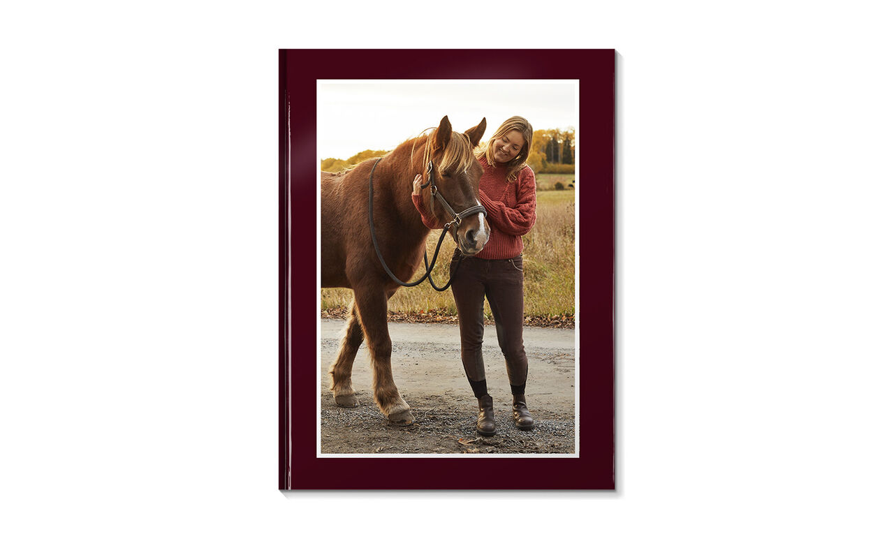 Una ragazza sta accanto a un cavallo in un prato e sorride. Indossa un pullover rosso.