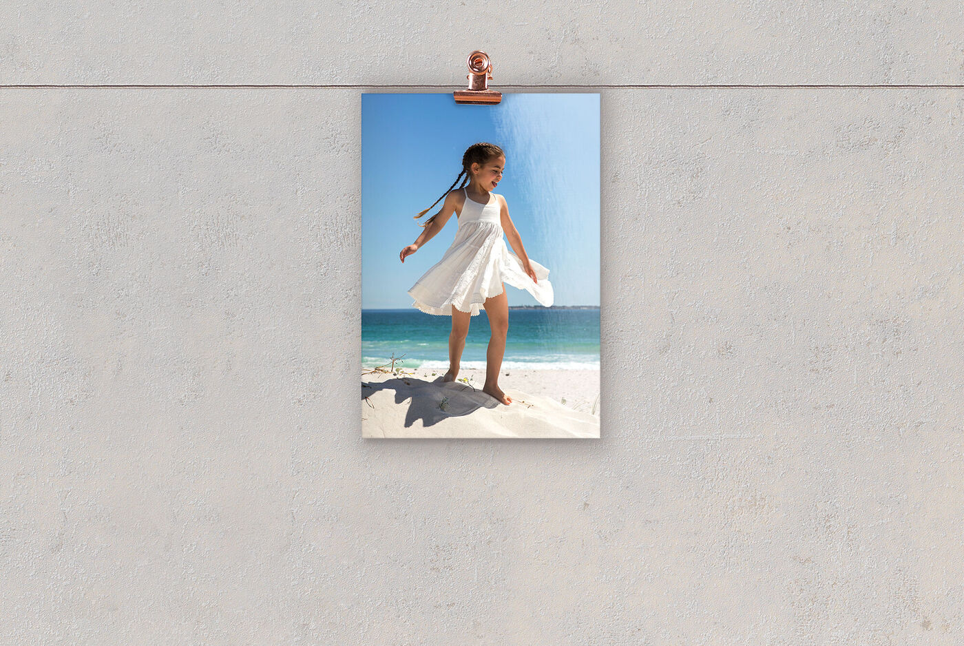 Una ragazza felice in un vestito bianco si trova su una collina di sabbia in spiaggia. Dietro di lei si vede il mare blu e il cielo.