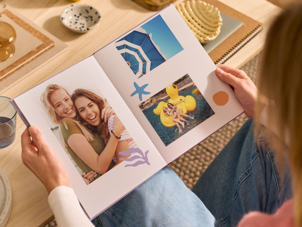 Una donna è seduta su un divano in salotto, con in mano un FOTOLIBRO CEWE aperto.
