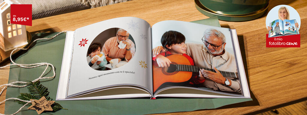 Due bambini sono seduti a un tavolo e guardano un fotolibro. Uno tiene una tazza in mano. Sfondo con decorazioni natalizie.